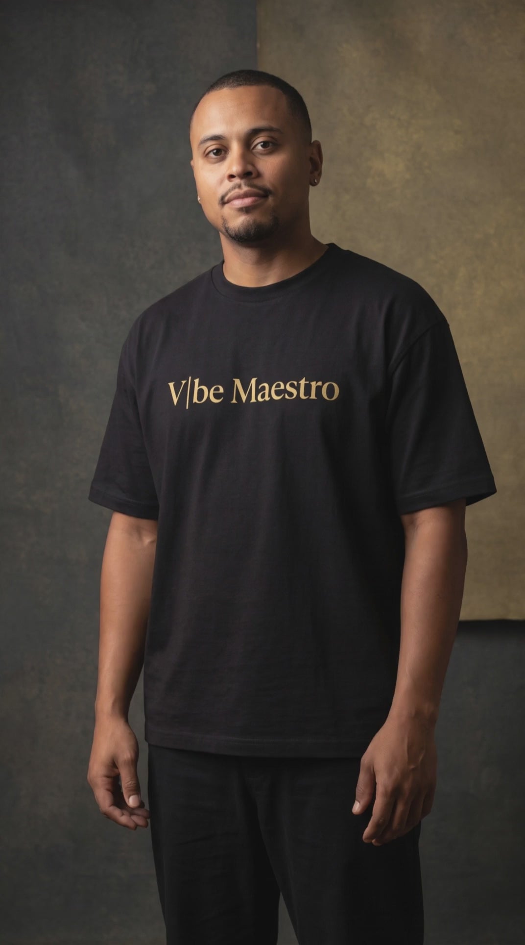 Load video: Model wearing a black Vibe Maestro T-shirt in a moody editorial studio.